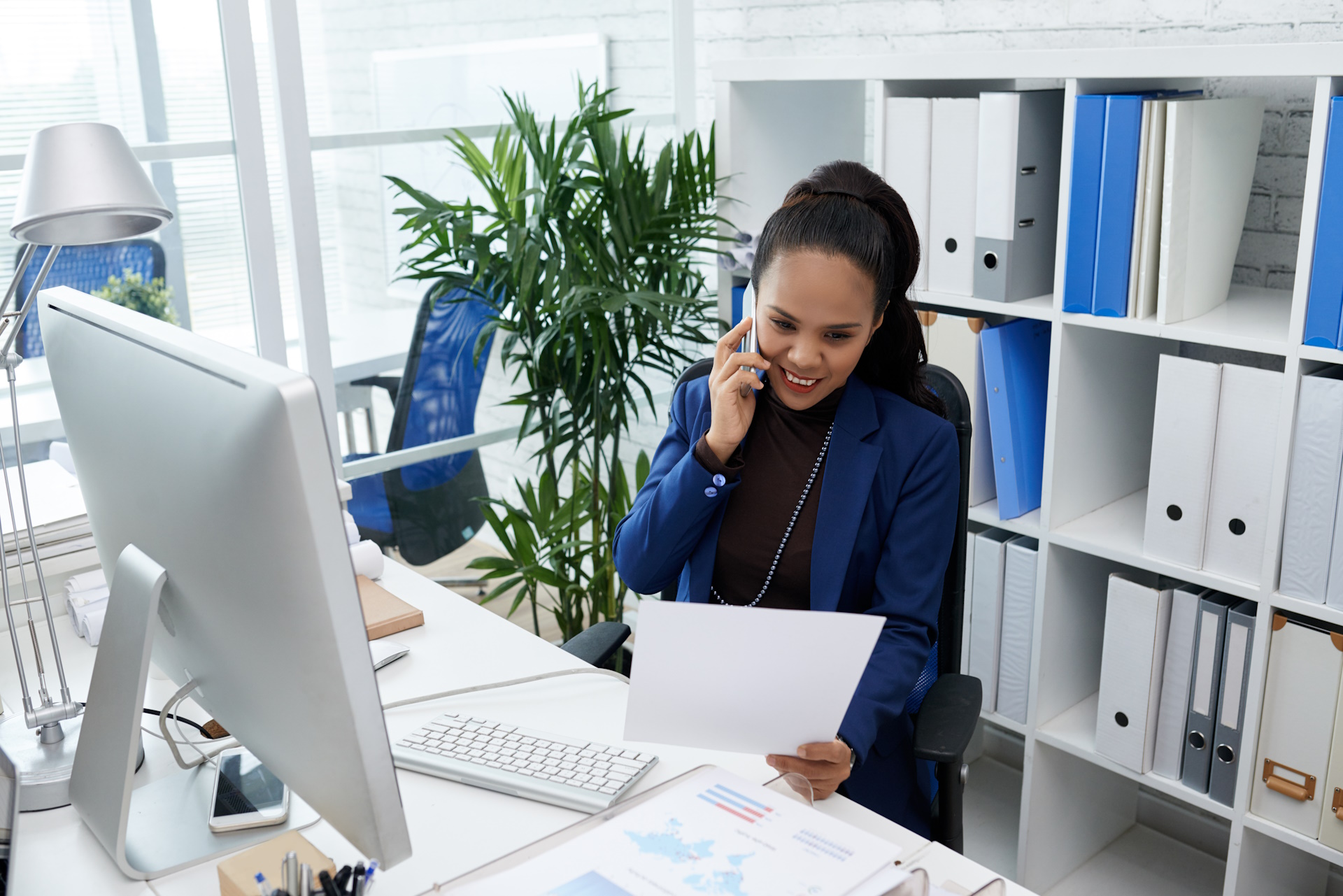 Portrait of cheerful business lady reading document and calling on the phone